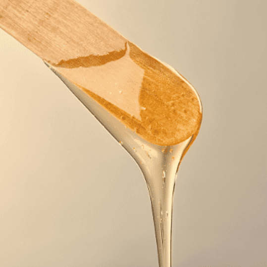 Wooden stick with honey dripping off the end against a beige background.