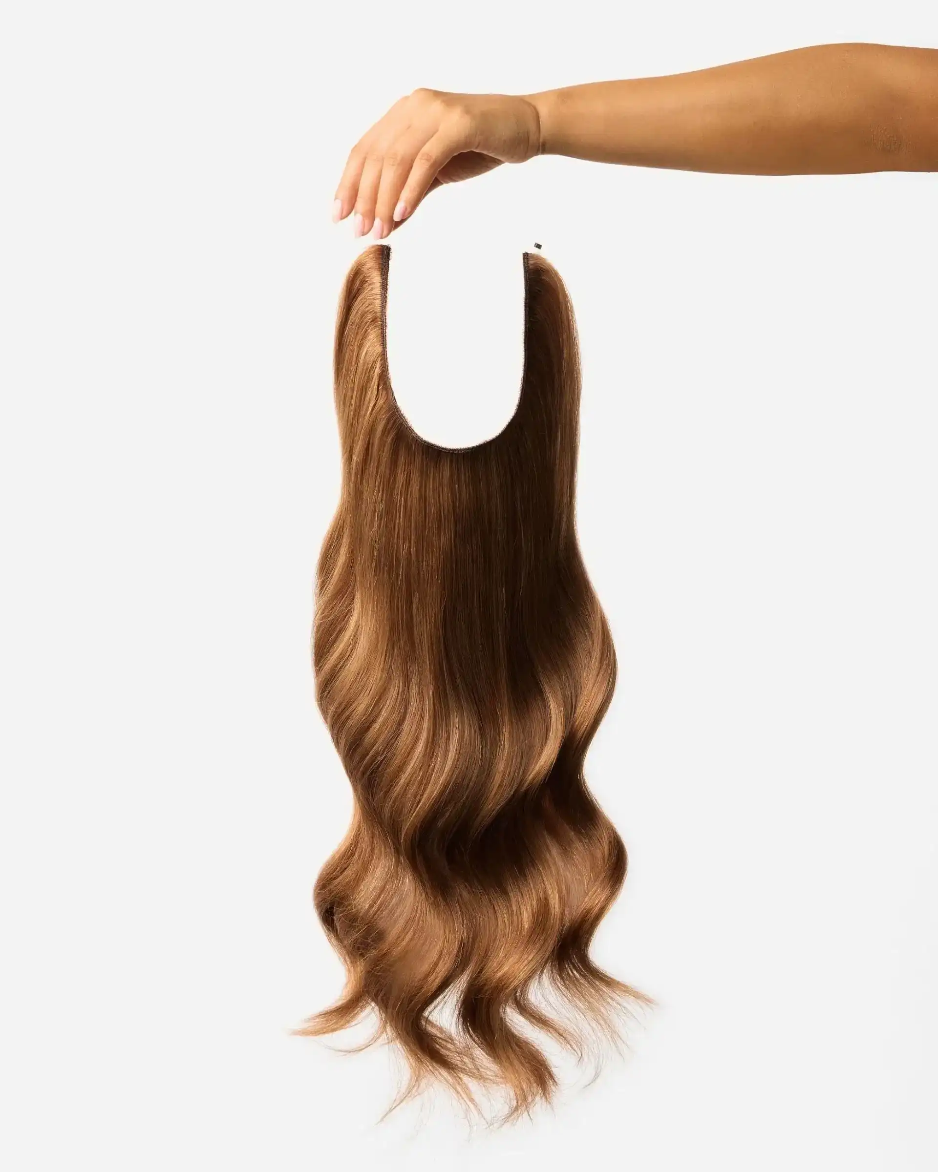 Hand holding a wavy brown hair extension against a plain white background.